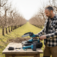Man in an orchard with tools on a table, surrounded by leafless trees.